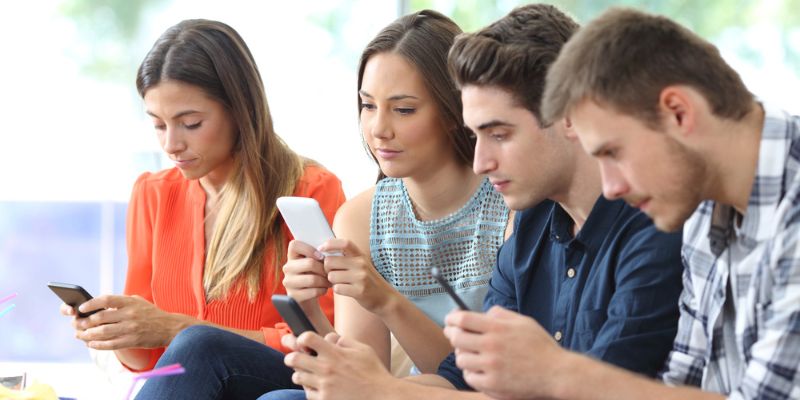 Four people engrossed in their mobile devices in a casual setting.